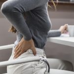 Eine Frau am Arbeitsplatz hält sich die Hand an den schmerzenden Rücken